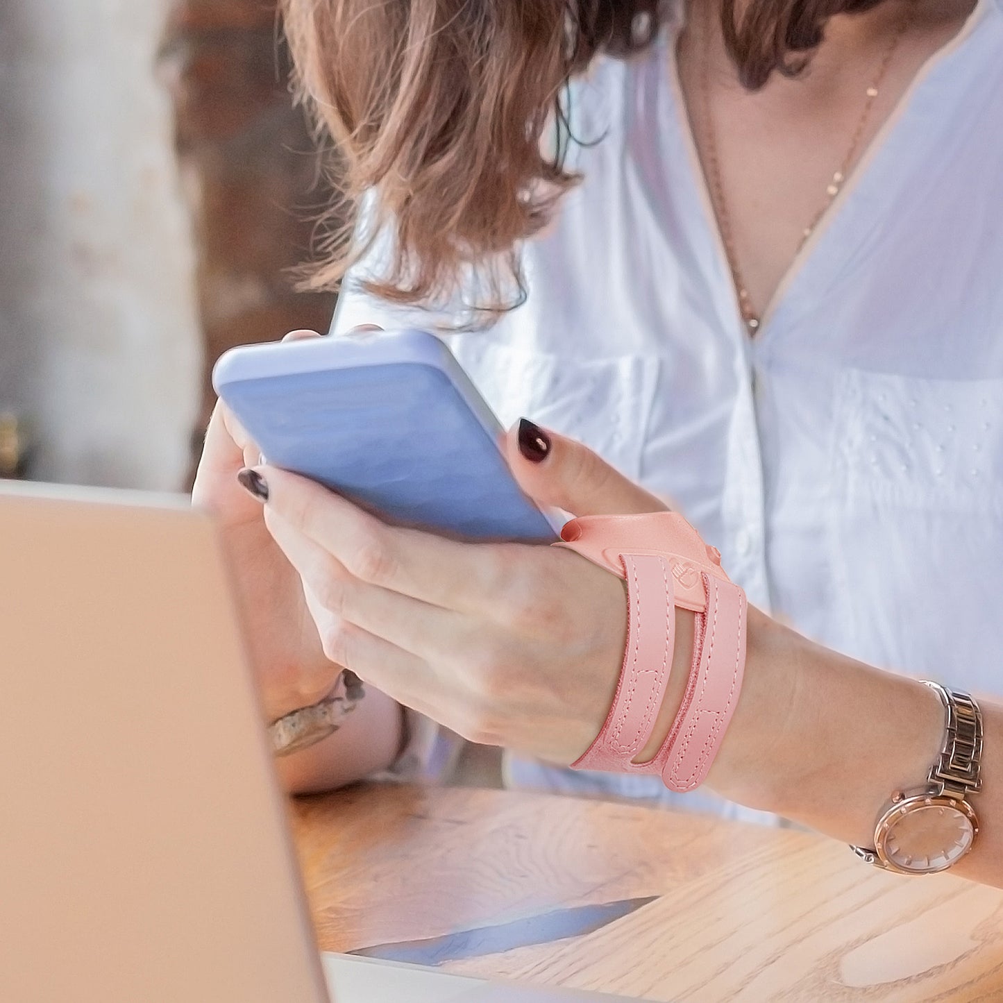 Person wearing a pink thumb brace while using a smartphone at a desk, demonstrating comfortable daily use.
