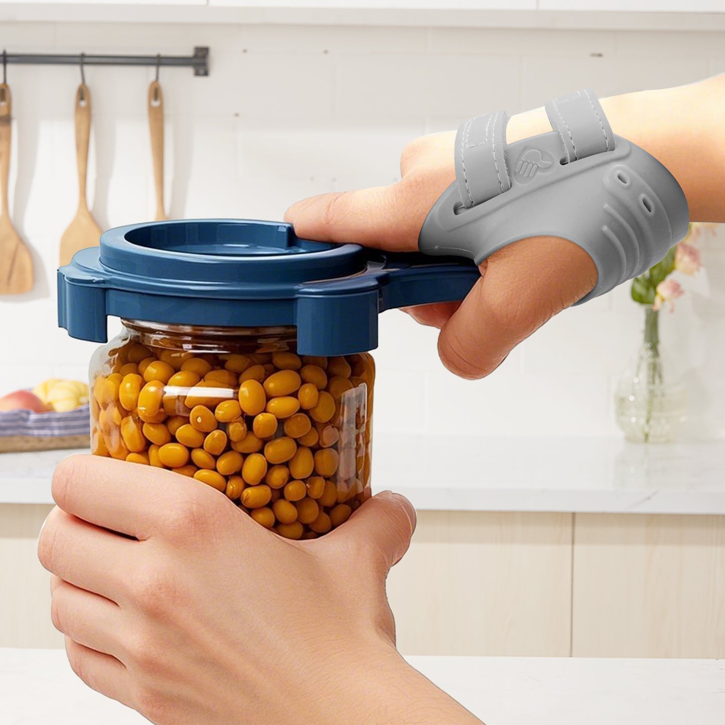 A close-up of a person’s hands in a kitchen: one hand wears a gray thumb brace and grips a blue jar opener attached to a glass jar lid, while the other hand holds the jar, showing the brace provides support for opening jars.
✨ 精简版 Alt Text（适合平台字符限制）